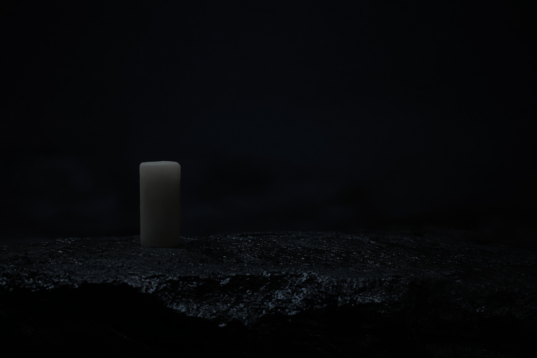 A single unlit candle standing in a nearly dark room
